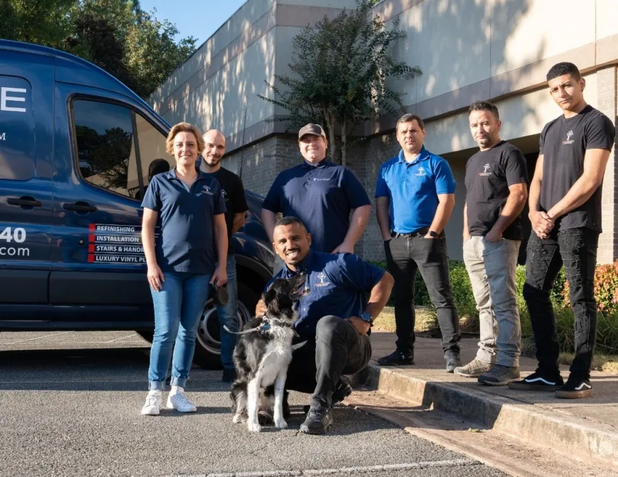Team of seven hardwood flooring professionals posing outside their office with a company van and a dog on a sunny day
