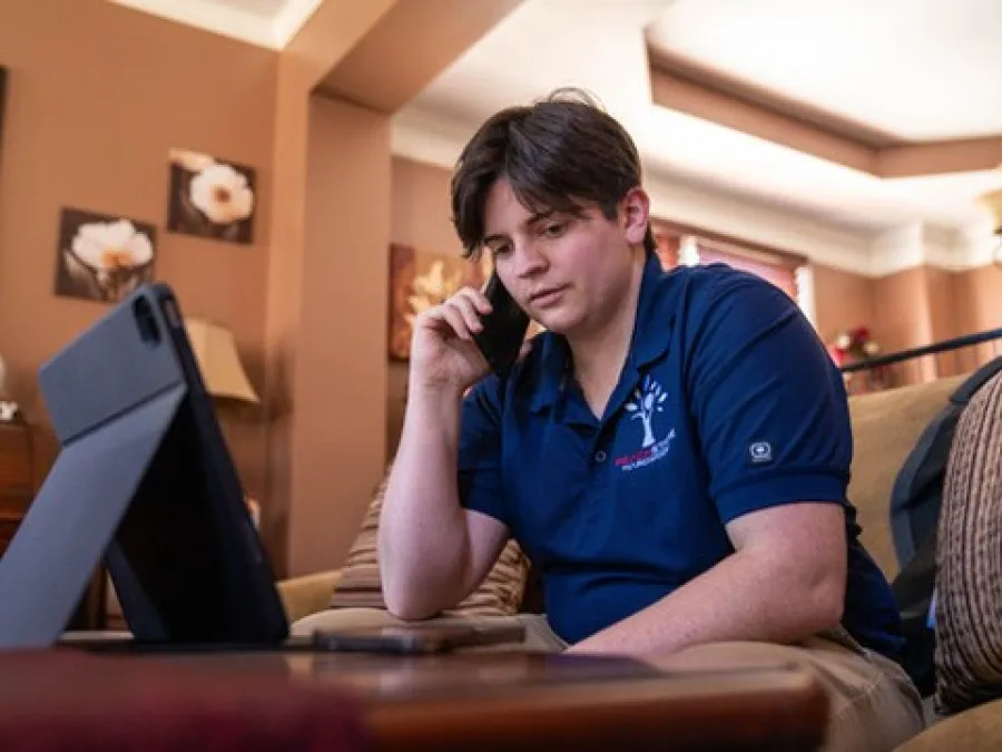 Young man sitting on couch using smartphone and tablet in cozy living room with warm lighting.