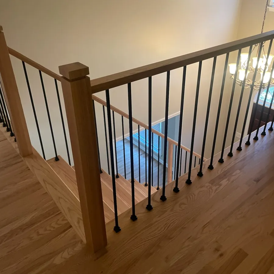 Wooden staircase with black metal railings and a chandelier in a well-lit modern home interior.