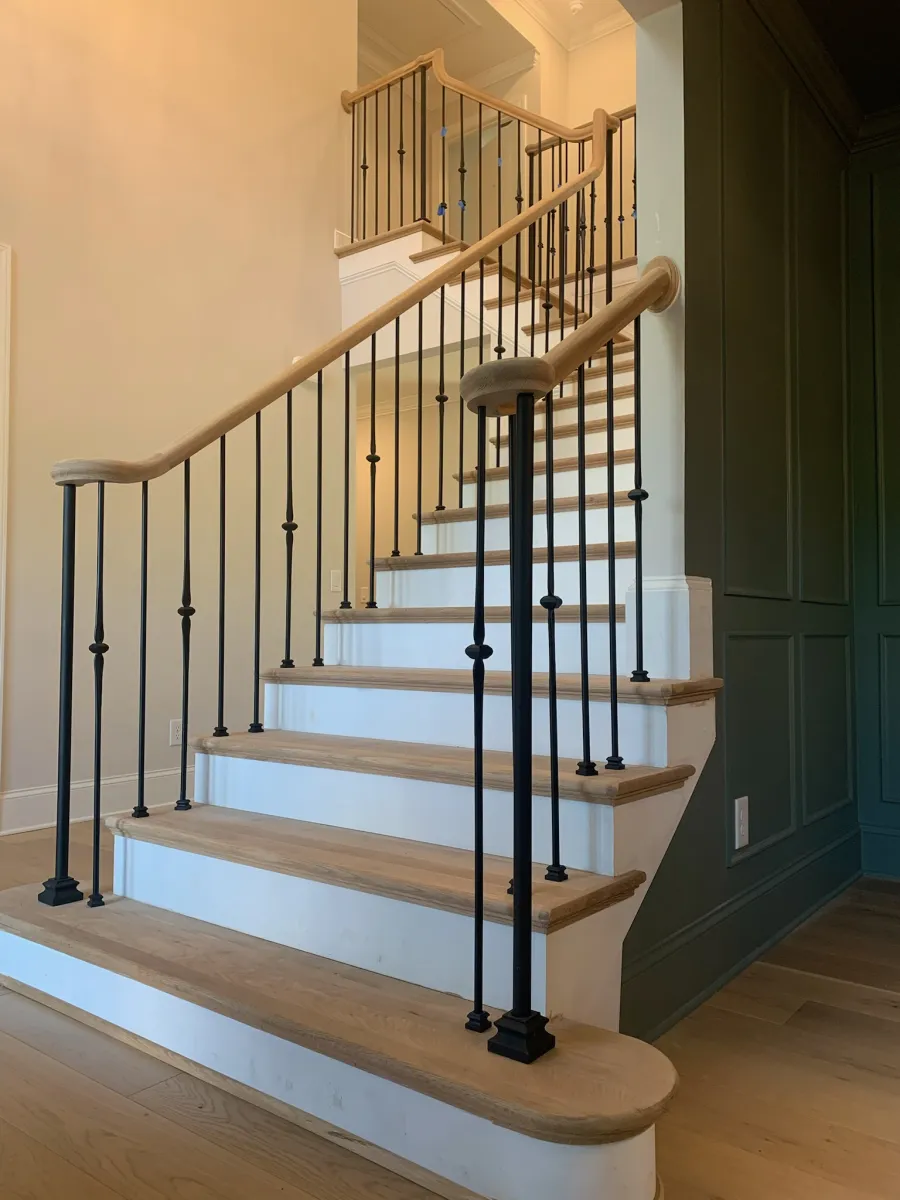 Wooden staircase with white risers and black metal balusters in a modern home interior.