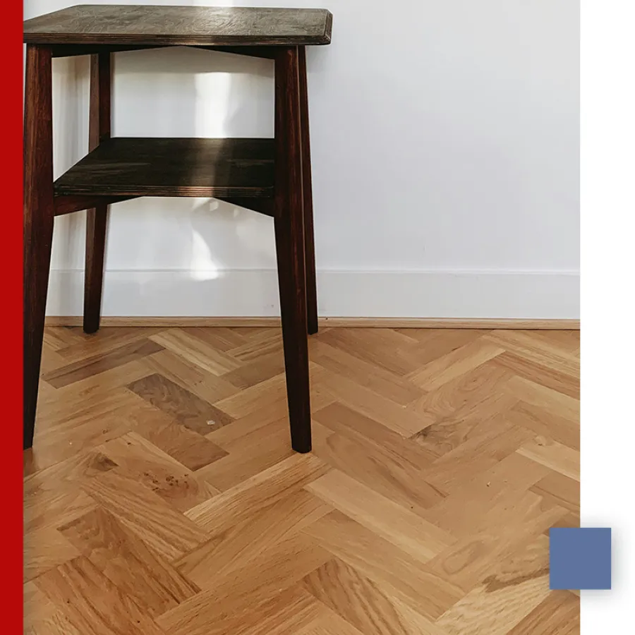 Dark wooden chair legs on a light herringbone patterned hardwood floor against a white wall with baseboard.