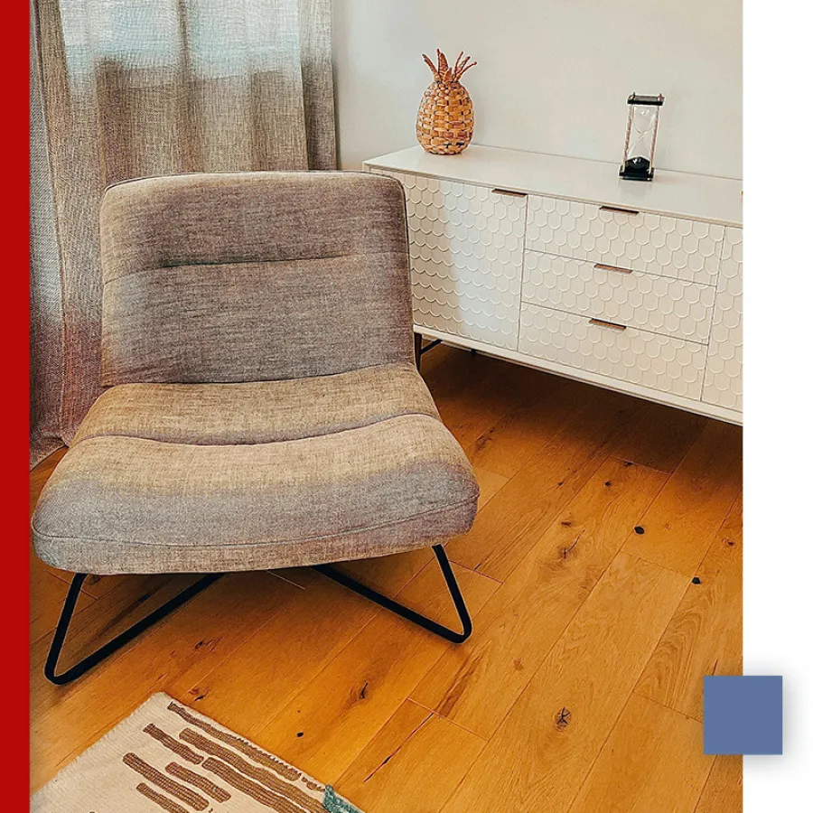 Cozy gray cushioned chair on wooden floor beside white textured cabinet with decorative items.