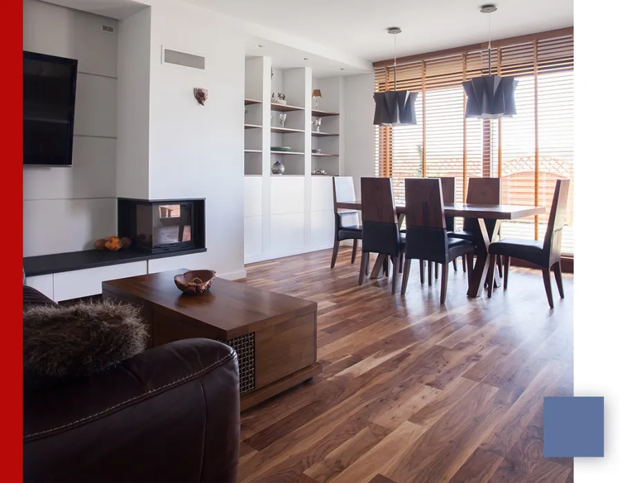 Modern dining and living area with wooden floors, dark furniture, fireplace, and large windows with blinds.