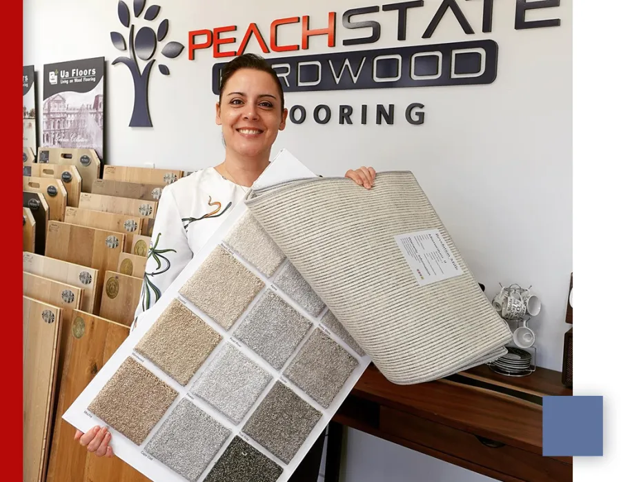 Smiling woman holds carpet samples in showroom with wood flooring displays and Peach State Hardwood sign