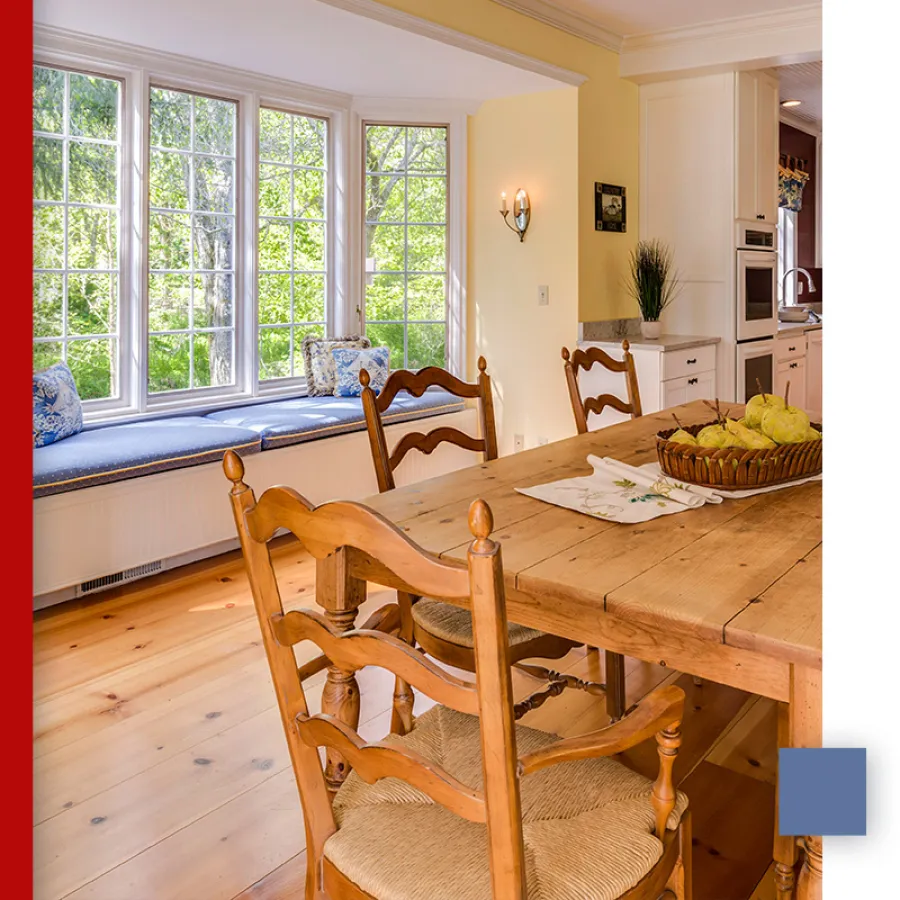 Bright kitchen dining area with wooden table and chairs, window bench seating with blue cushions, and natural light.