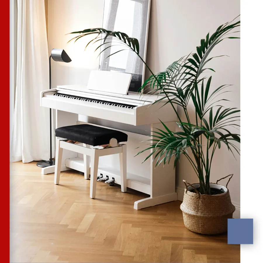 White digital piano with black bench next to large green potted plant and floor lamp in cozy room.