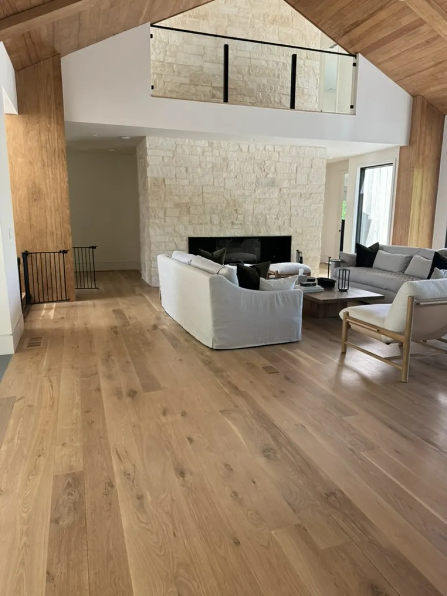 Spacious living room with wooden floors, vaulted ceiling, stone fireplace, and modern white and gray sofas.
