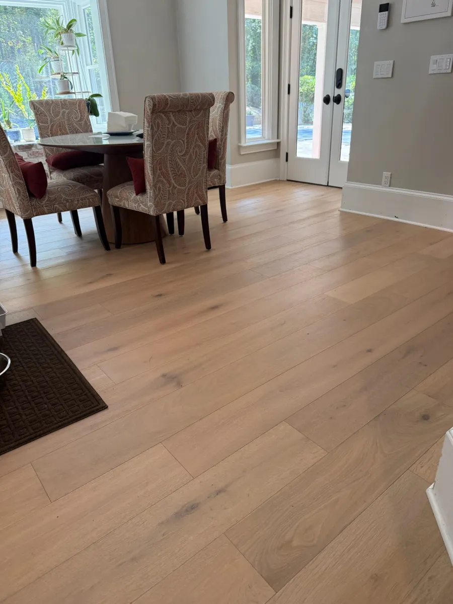 Dining area with patterned chairs around a round glass table on light wooden flooring near glass doors.