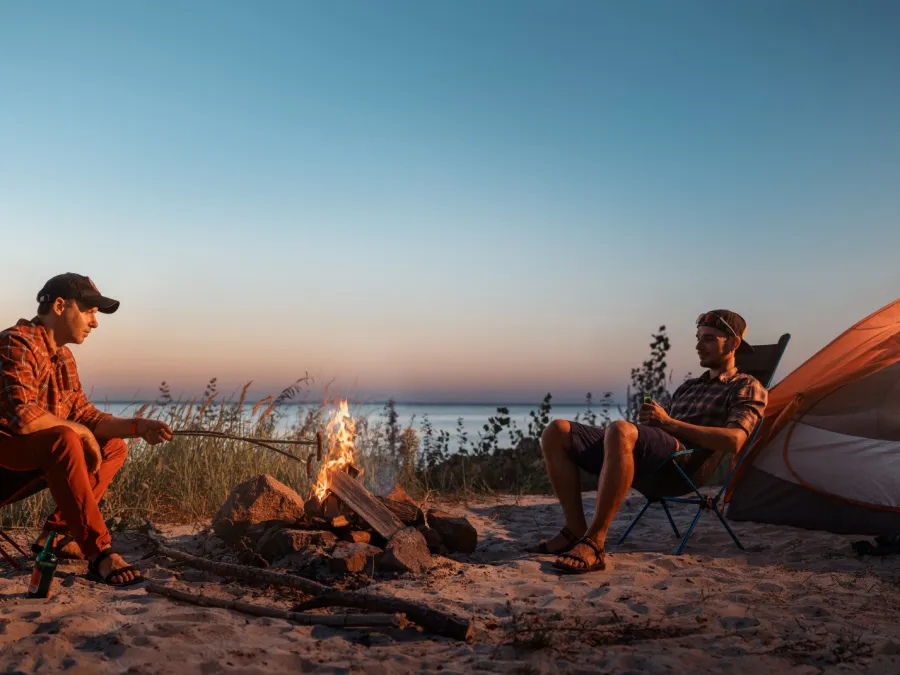 a couple of men sitting on a campfire by a lake