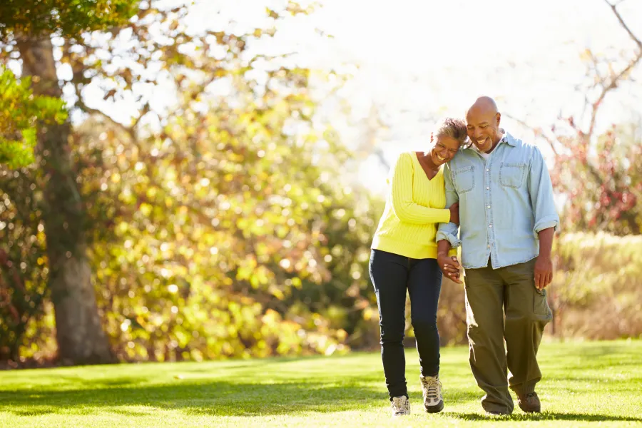 Couple walking outdoors in autumn holding hands and smiling with trees and grass in the background