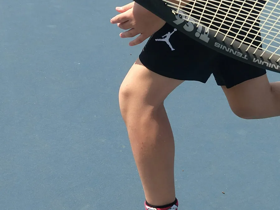 Close-up of a tennis player's leg and arm in motion on a blue court, holding a racquet.