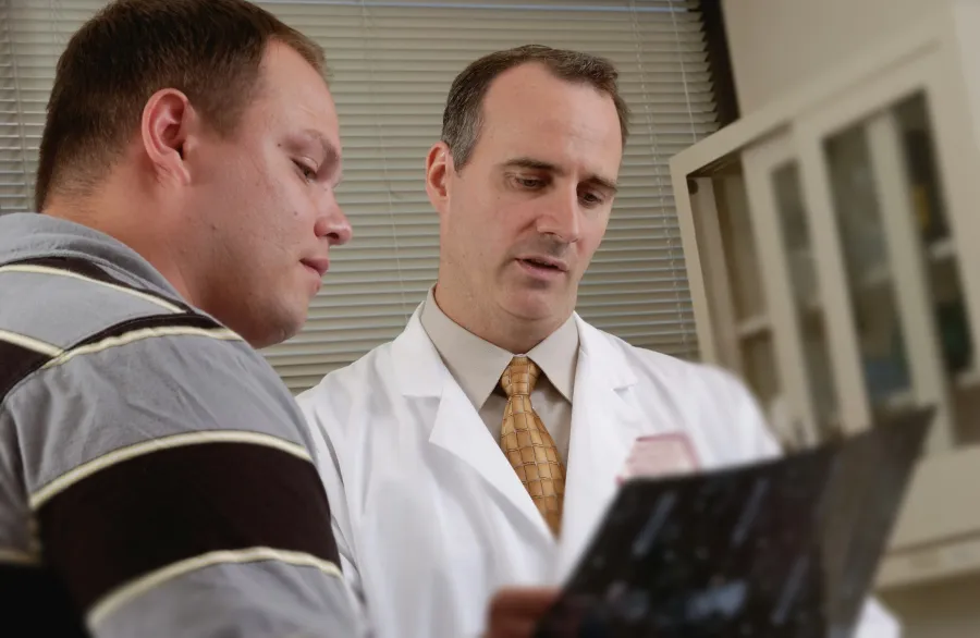 Doctor in white coat explaining medical results to a patient in a consultation room with blinds in background