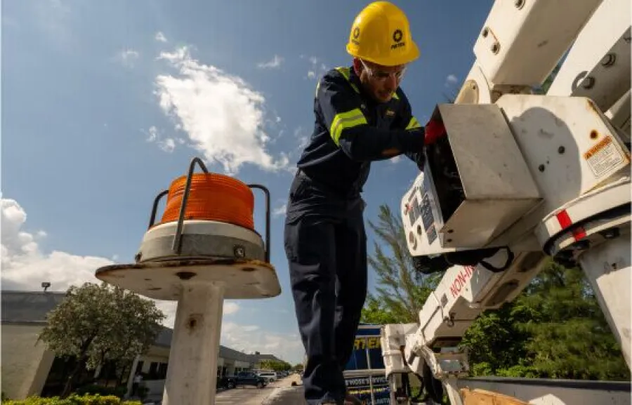 Electrician wearing safety gear working on utility bucket truck under blue sky with orange cable spool nearby