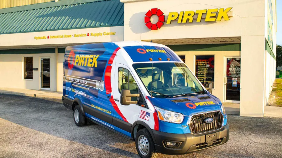 Blue and white Pirtek service van parked outside a Pirtek hydraulic and industrial hose service center.