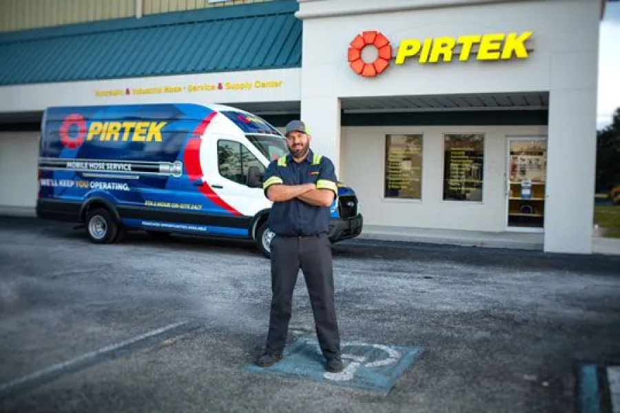Technician standing in front of Pirtek service van and store signage wearing uniform at the repair center.