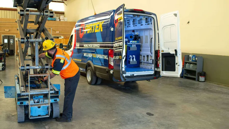Worker in safety gear operating machinery near an open service van in a warehouse workshop environment