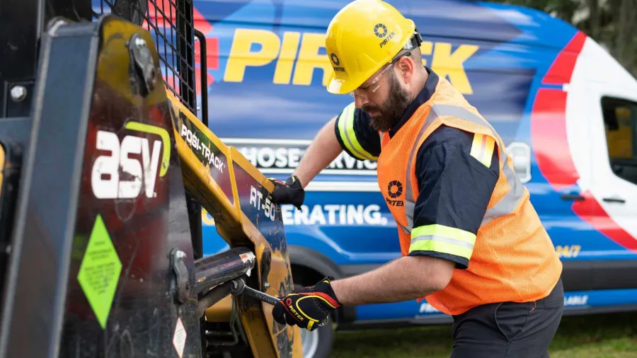 Construction worker in safety gear operating machinery with branded van visible in the background.