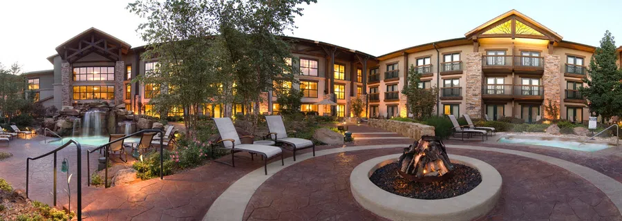 Luxury lodge at dusk with outdoor pool, waterfall, lounge chairs, fire pit, and warm glowing windows.