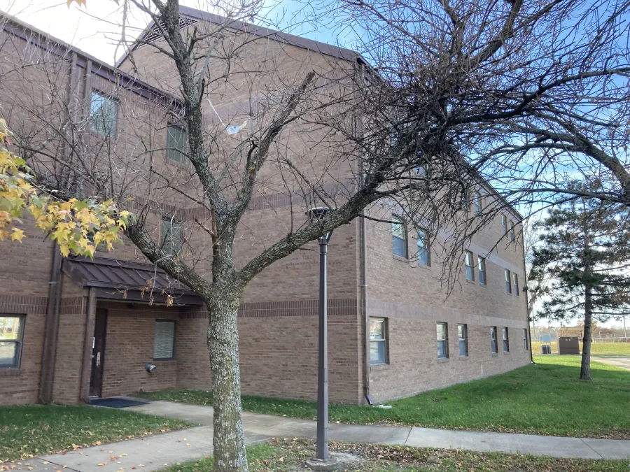 Two-story brick building with leafless tree and lamppost in front on a clear fall day.