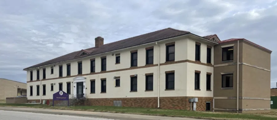 Two-story beige office building with dark windows and a sign in front under a cloudy sky.