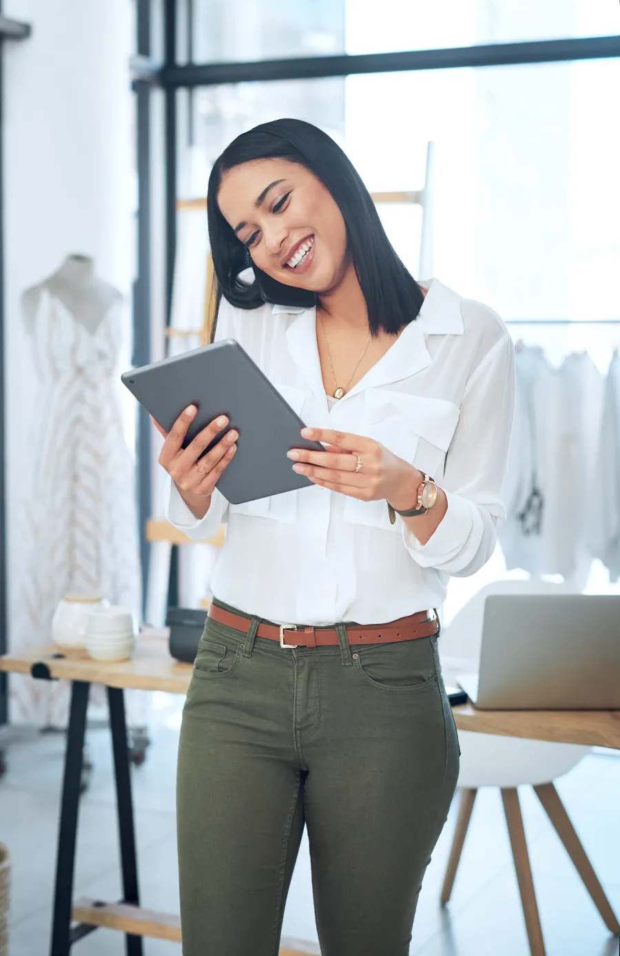 Smiling woman in a professional setting, working on a laptop at a modern desk.