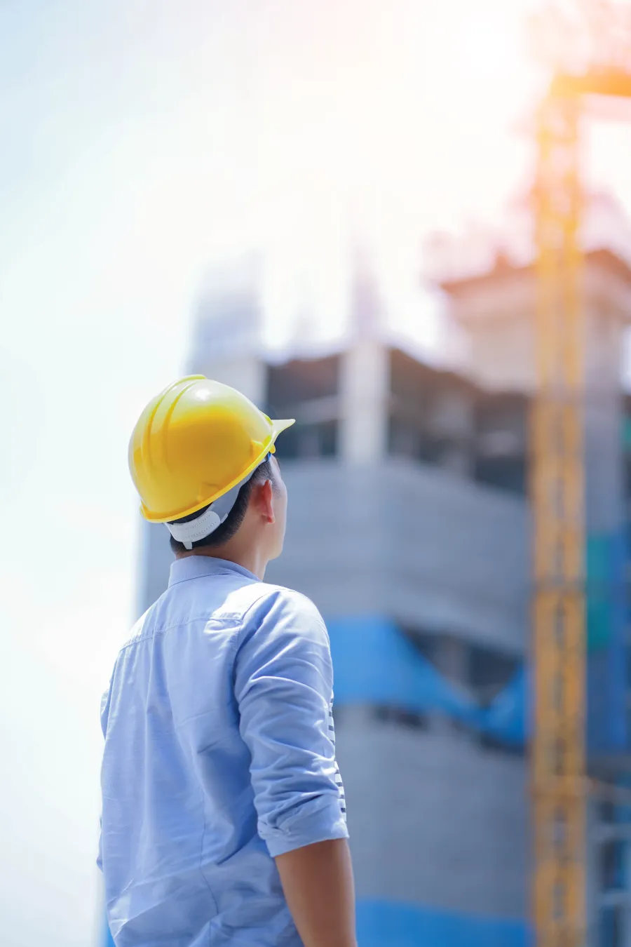 Construction worker in yellow helmet inspects building site under bright sunlight at mid-day.