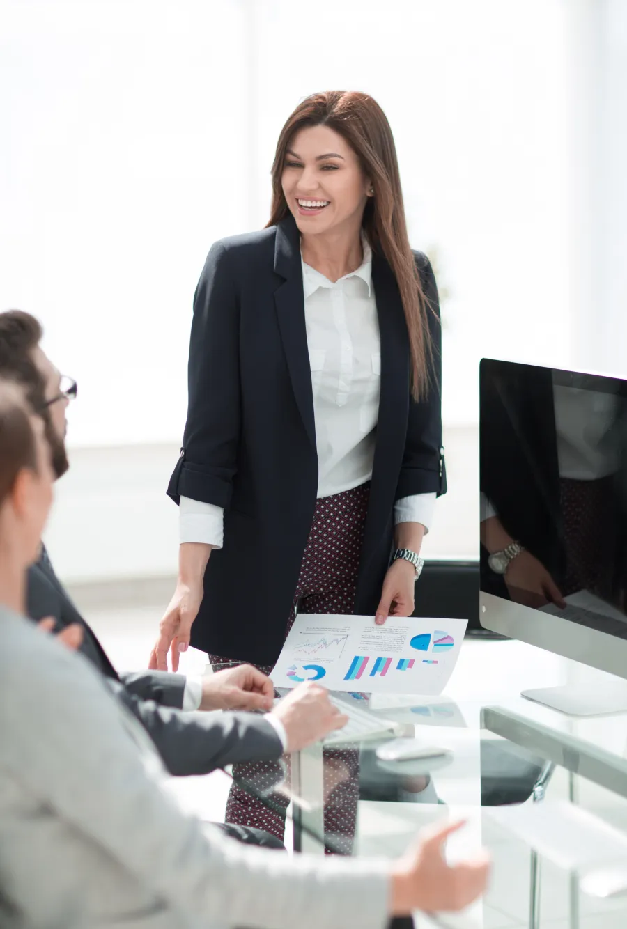 Businesswoman presenting charts during meeting with colleagues around a glass table in office.
