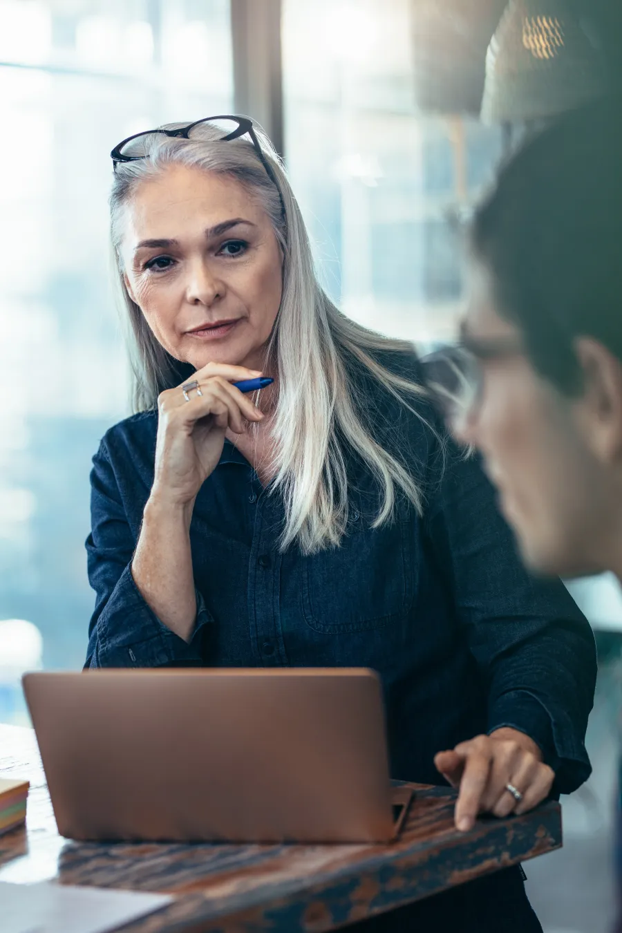 Smiling woman in a professional setting, working on a laptop at a modern desk.