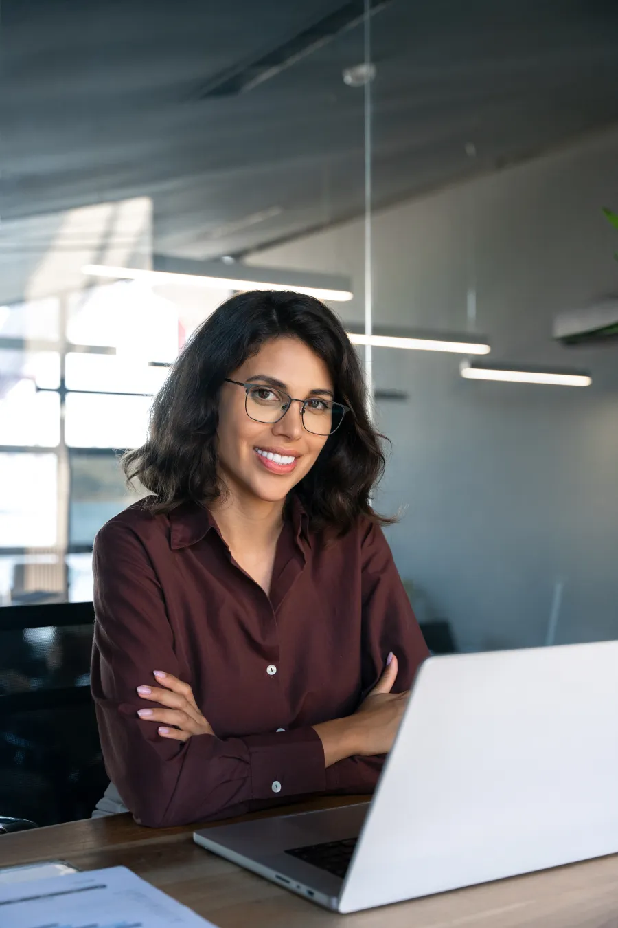 Smiling woman in a professional setting, working on a laptop at a modern desk.
