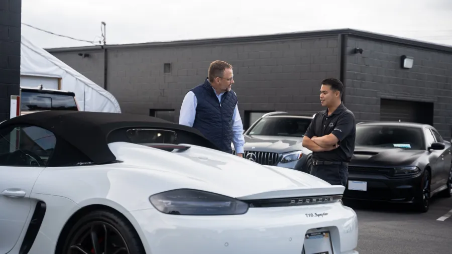 a couple of men standing next to a white car in a parking lot