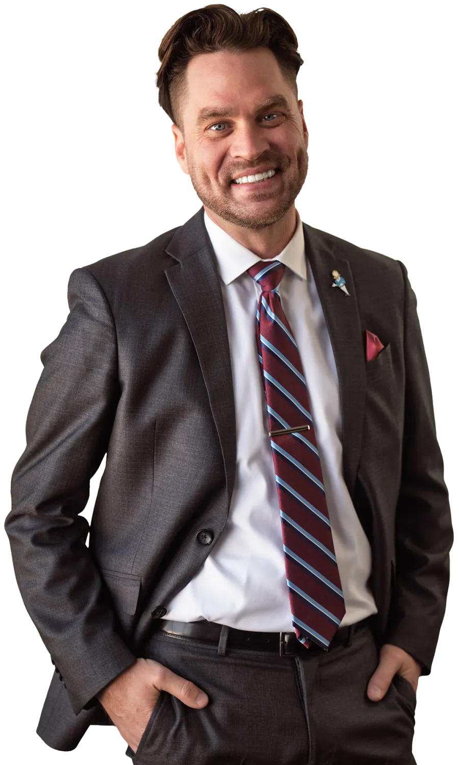 Smiling man in dark suit with striped tie and hands in pockets standing confidently with a friendly expression