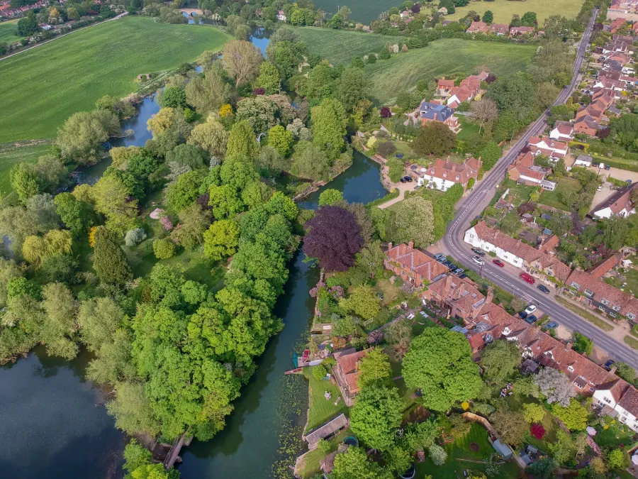 Aerial view of a river winding through lush greenery beside a village with houses and roads under clear weather.