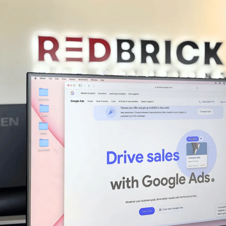 Laptop displaying Google Ads page promoting driving sales, with blurred RedBrick sign in background