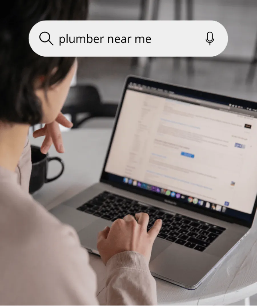 Person searching for plumber near me on laptop with search bar overlay and coffee mug nearby