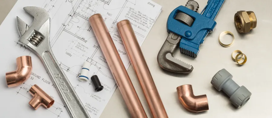 Copper pipes, plumbing tools, fittings, and blueprints laid out for plumbing installation work.