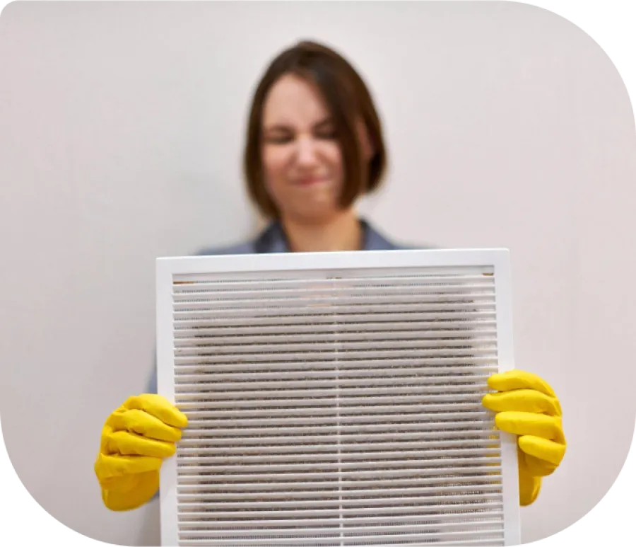 Woman wearing yellow gloves holding a dirty air filter with a displeased expression indoors