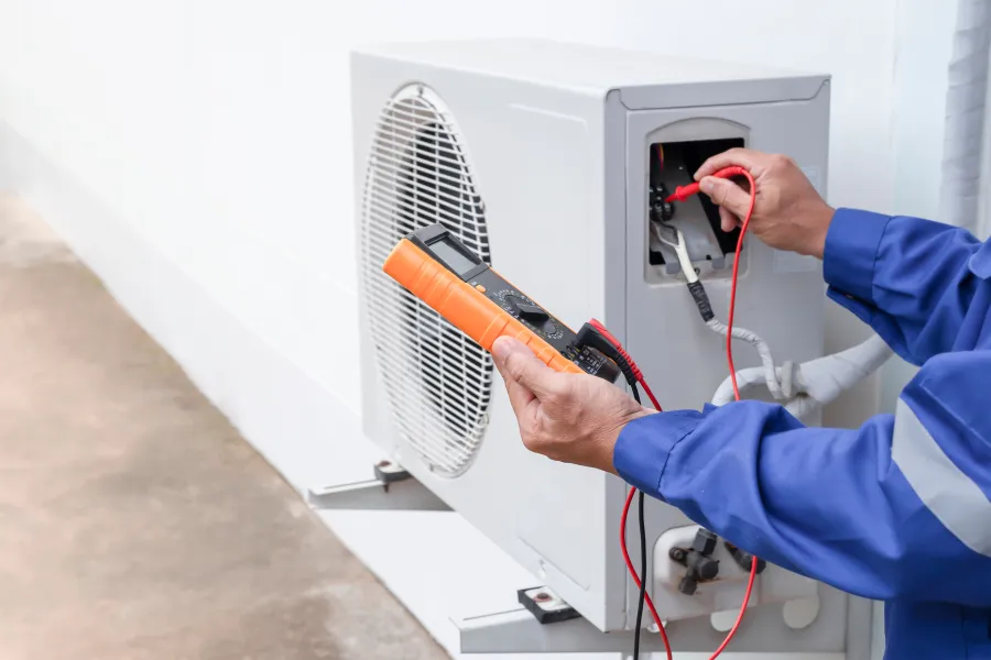 Technician testing and repairing an outdoor air conditioning unit using a multimeter device and probes.