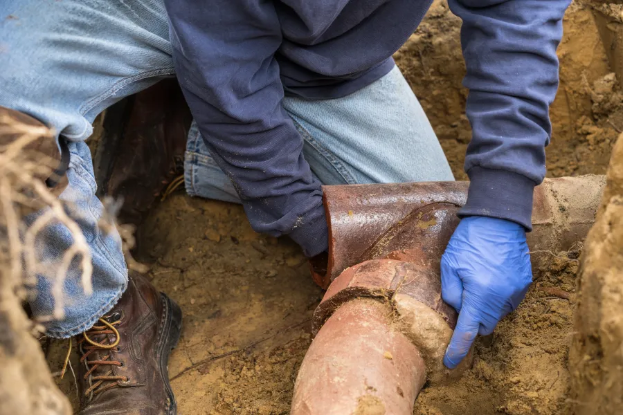 Black drainage pipe laid in a narrow trench surrounded by soil and grass during installation work.