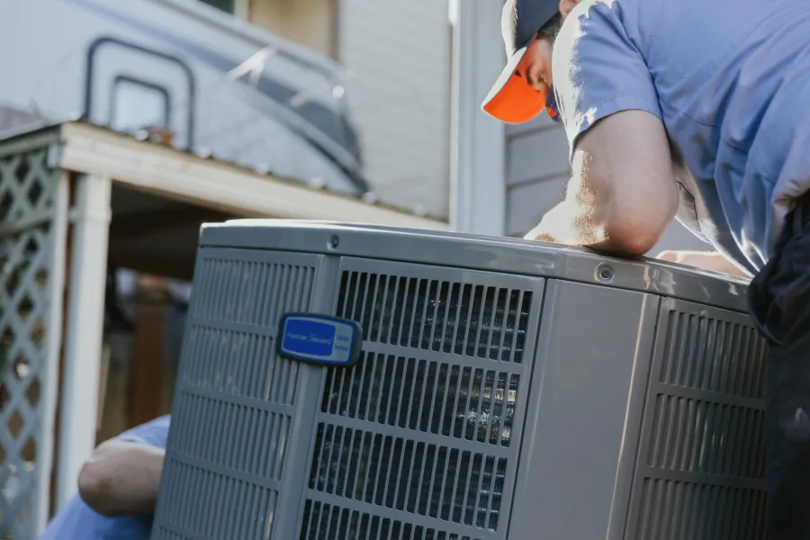 Technician inspecting and repairing an outdoor air conditioning unit on a residential property.