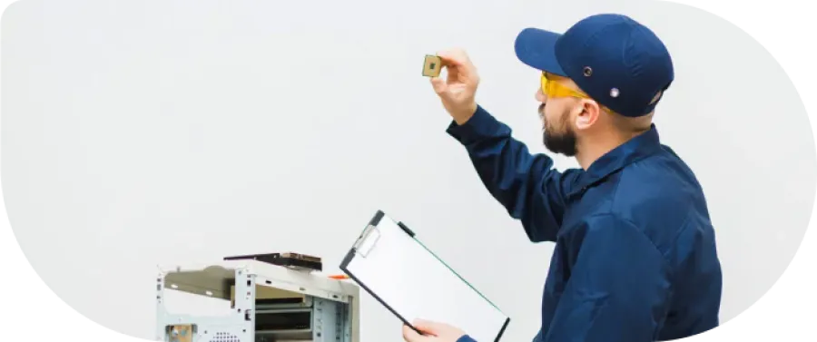Technician in blue uniform inspecting a computer processor chip with a clipboard beside an open computer case.