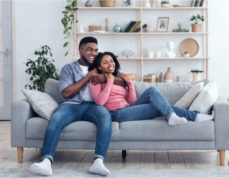Happy African American couple relaxing on gray couch in cozy modern living room at home