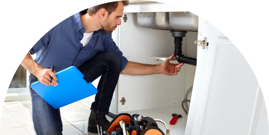 Plumber inspecting kitchen sink pipes with clipboard and tool bag for repairs and maintenance.