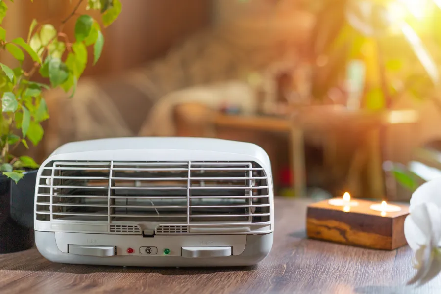 Compact white air purifier on a wooden table with candles and plants in a cozy, sunlit room.