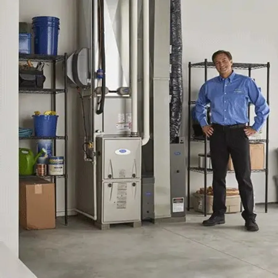 Technician standing next to a modern furnace and water heater in a clean basement with storage shelves.