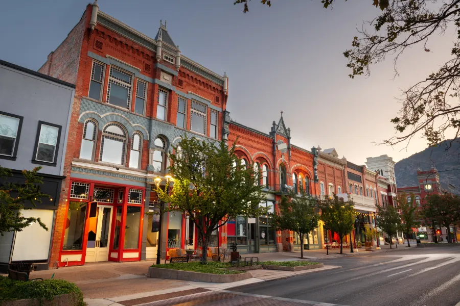 Historic red brick buildings with ornate facades line a quiet downtown street at dusk with trees and street lamps.