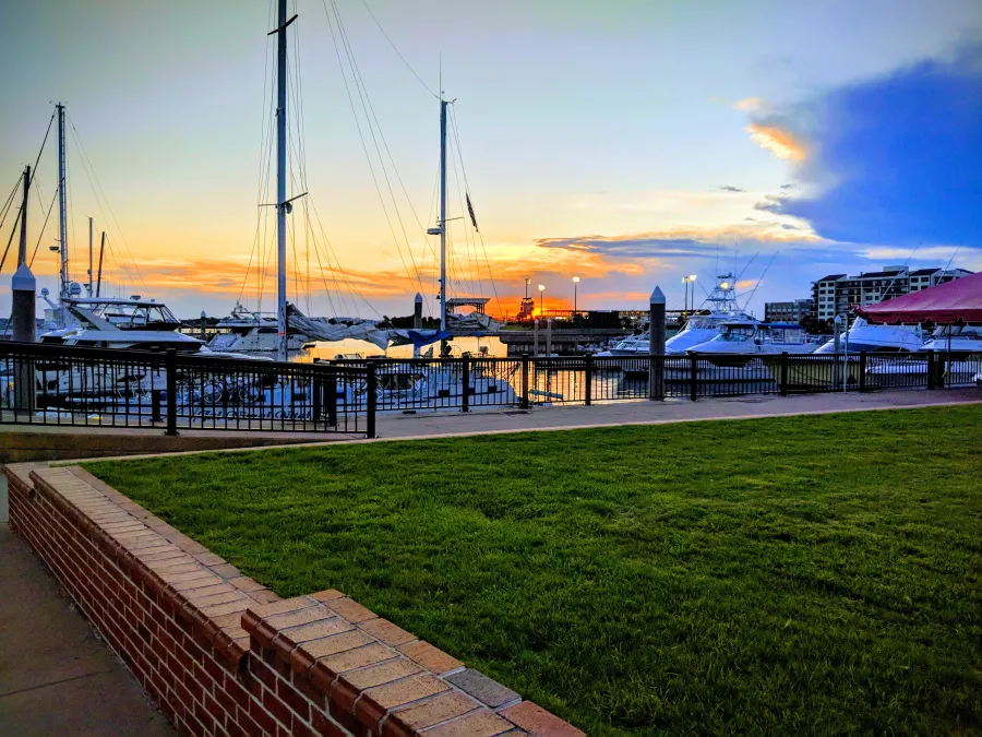Marina boats docked by waterfront with grassy lawn and vibrant sunset sky in the background.