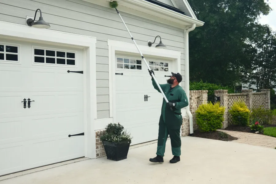 pest tech working on a house exterior near garage doors.