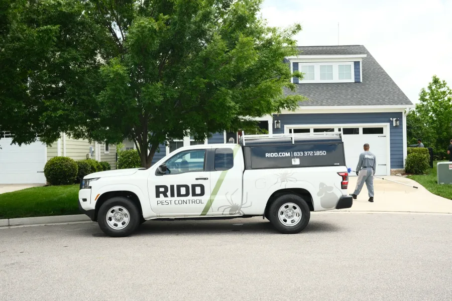 RIDD Pest Control white pickup truck parked on suburban street next to technician walking towards house.