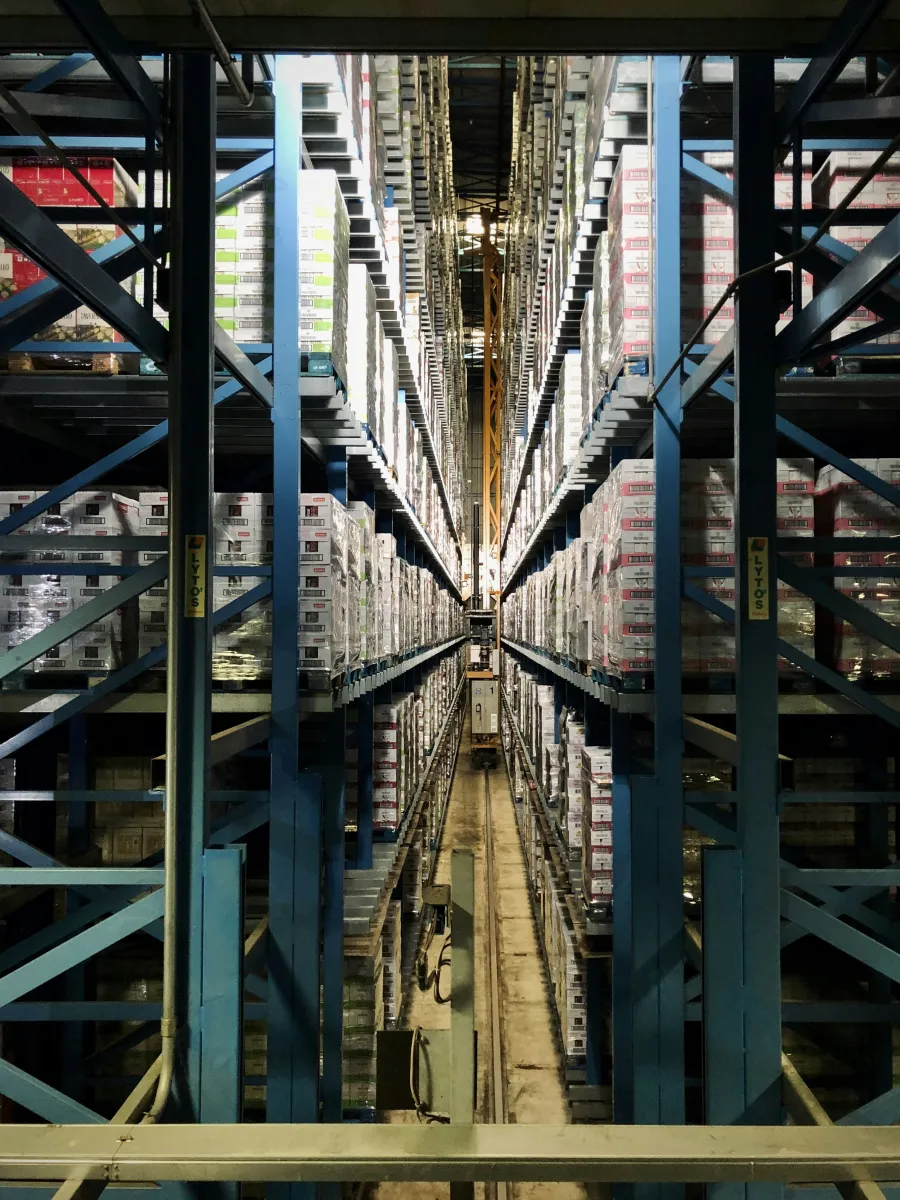 High shelves stocked with boxed goods in a large warehouse with automated retrieval system in center aisle