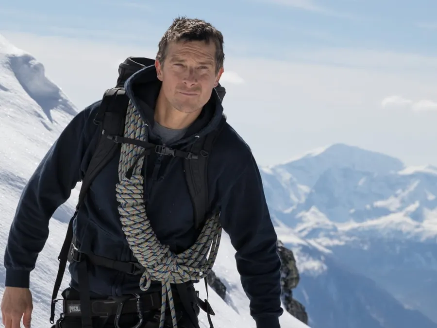 Man in climbing gear with rope climbs snowy mountain with snowy peaks in the background under blue sky